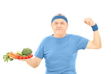 Mature man holding plate full of vegetables and showing strength