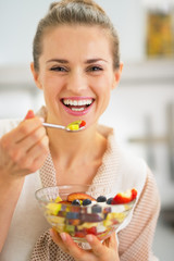 Smiling young woman eating fresh fruit salad