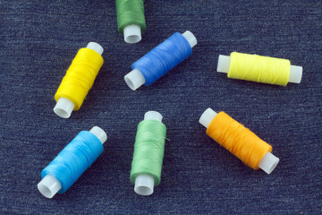 Spools with color threads on blue jeans fabric background