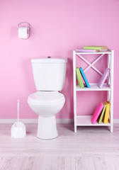 White toilet bowl and stand with books, on color wall