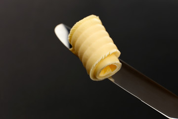 Curl of fresh butter on knife on grey background