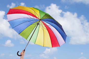 Rainbow umbrella in woman hands against cloudy sky