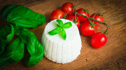 Ricotta with basil and cherry tomatoes on wooden table