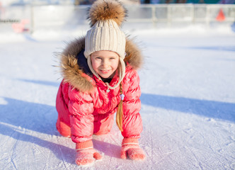 Happy adorable girl sitting on ice with skates after the fall