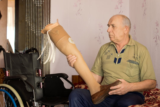 Elderly amputee sitting holding an artificial leg