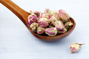 Rose tea buds in wooden spoon on pastel blue background