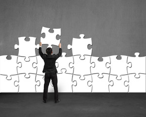 Businessman holding puzzle to assemble on concrete wall