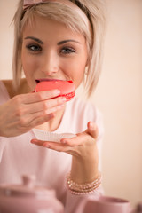 Young beautiful blond woman eating macaroon while having tea-par