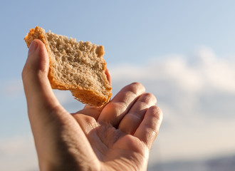 Fototapeta na wymiar Ręka trzymać kromkę chleba na tle nieba.