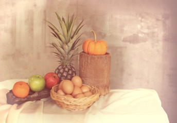 Still life apple, pineapple,pumpkin and basket of eggs in vintag