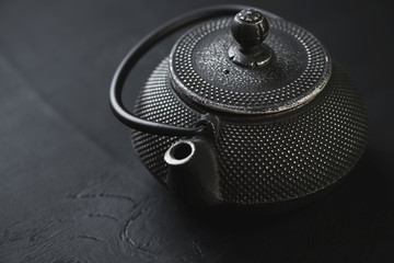 Obraz na płótnie Canvas Cast-iron asian teapot over black wooden surface, close-up