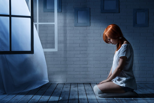 Lonely girl sits in an empty dark room opposite the window