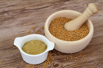 Mustard seeds in wooden mortar and mustard in white bowl