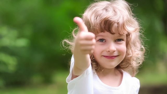 Happy child showing thumbs up outdoors in spring park