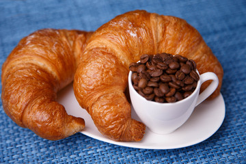 Two croissants and coffee beans in a tiny cup