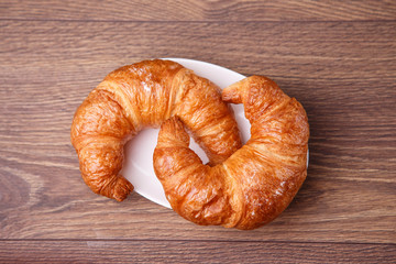 Two croissants on a plate with wooden background
