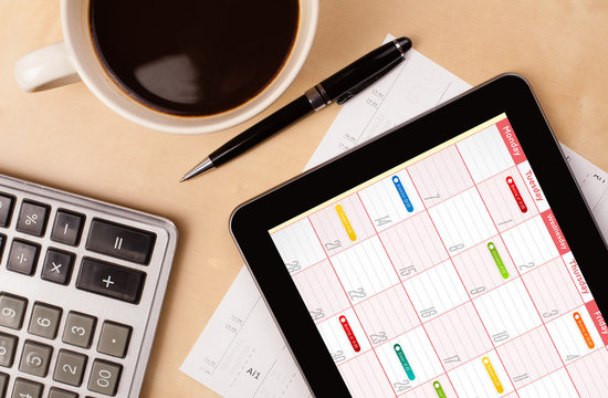 Tablet pc showing calendar on screen with a cup of coffee on a d