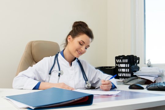 Cheerful young doctor woman in her office behind table