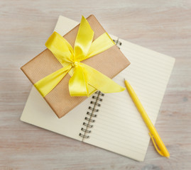 gift box with yellow bow and a notebook on a table