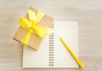 gift box with yellow bow and a notebook on a table