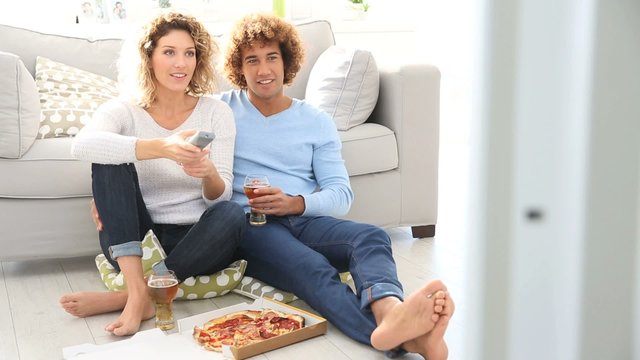 Cheerful couple at home having pizza in font of TV