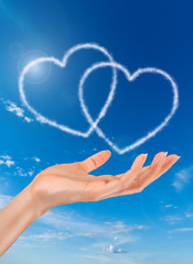 woman hand and heart shaped clouds on blue sky background
