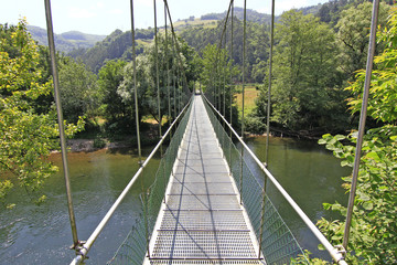 narrow suspension bridge over a river with lots of greenery