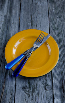 Empty Yellow Plate On Old Wooden Table With Blue Knife And Fork