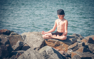 Naklejka na ściany i meble Young boy practising yoga on beach