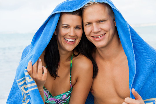 lachendes junges verliebtes paar mit einem handtuch am strand