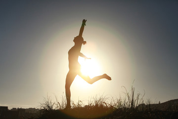 Silhouette of acrobatic teen gymnast balancing with the sun behi