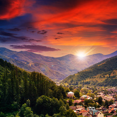 village on hillside meadow with forest in mountain at sunset