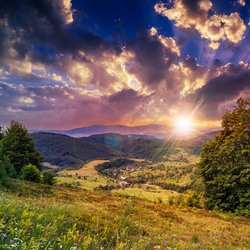 village on hillside meadow with forest in mountain at sunset