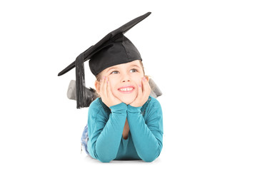 Adorable girl with graduation hat laying down and daydreaming