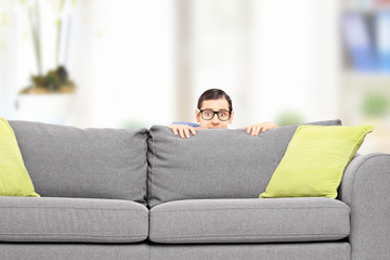 Frightened man hiding behind a sofa