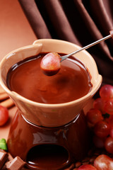 Chocolate fondue with fruits, on  brown background