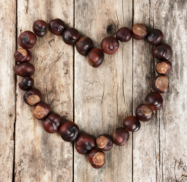 Chestnuts forming a heart on a wooden background