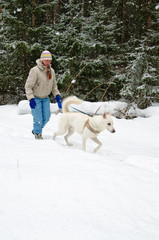 Woman with a white dog on a walk in the woods during a snowfall