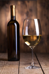 Black bottle of wine and wineglass on the wooden background .