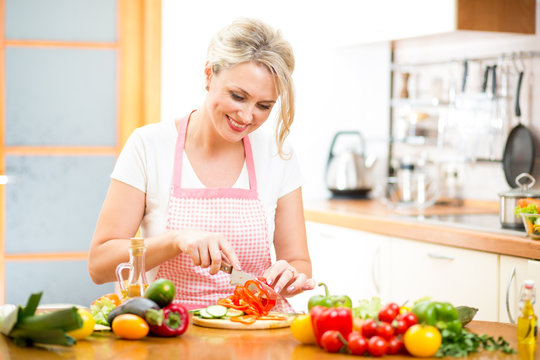 Cute woman cuts paprika for salad sitting at the kitchen table