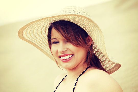 Smiling wonam in straw hat, sitting on beach.