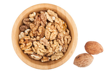 Cracked walnuts in wooden bowl with two nuts near isolated