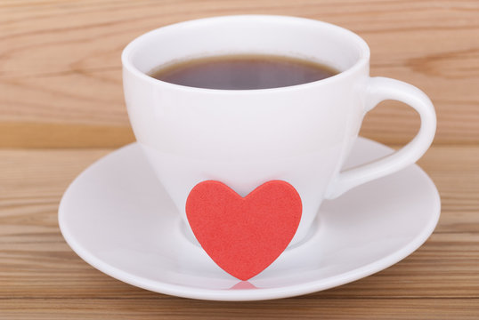 Cup of coffee and heart on wooden background.