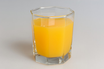 A glass filled with citrus juice on gray background