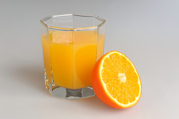 A half of orange with a glass filled with citrus juice on gray