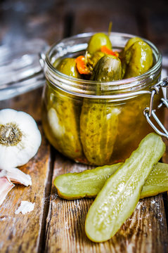 Pickles with garlic in glass jar on rustic wooden background