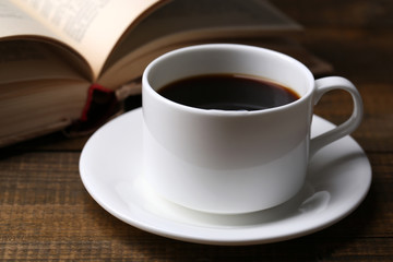 Cup of hot coffee with book on wooden background