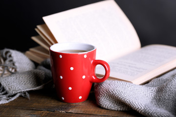 Cup of hot tea with book and plaid on table on gray background