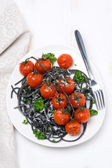 black spaghetti with roasted tomatoes and parsley, top view