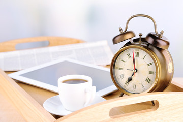 Tablet, newspaper, cup of coffee and alarm clock on wooden tray